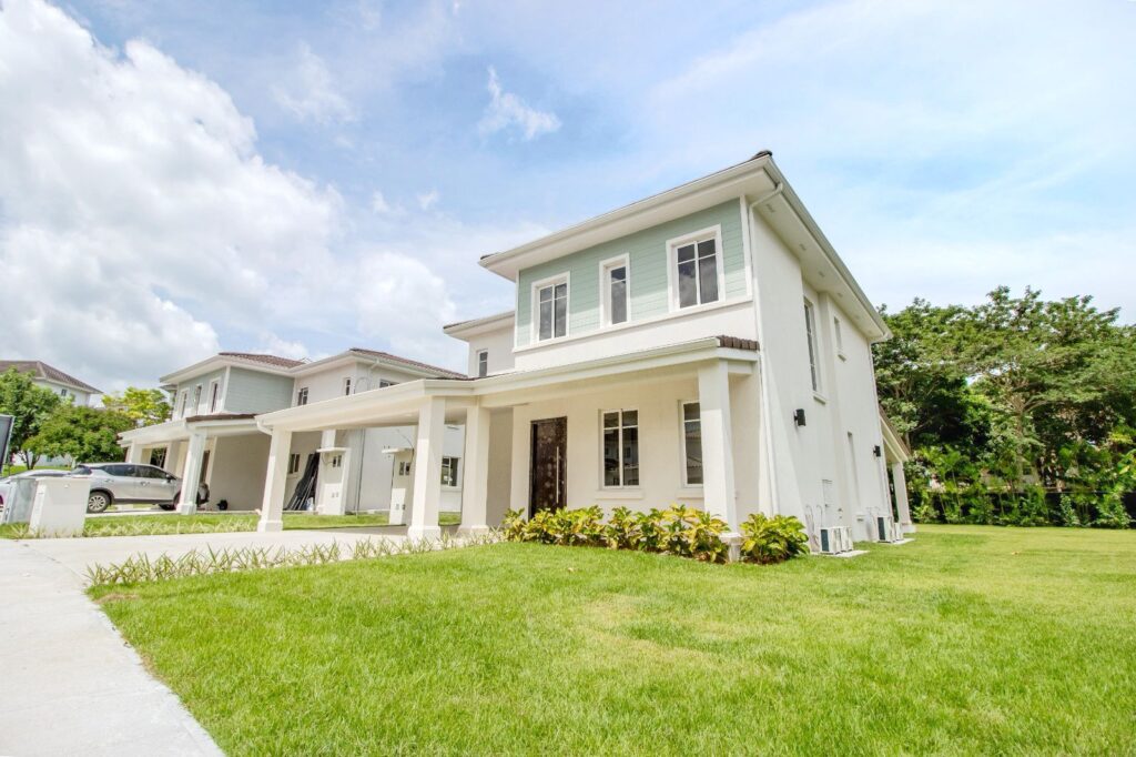 Modern two-story house with light green trim, white facade, and a covered porch, set on a well-manicured lawn under a blue sky.