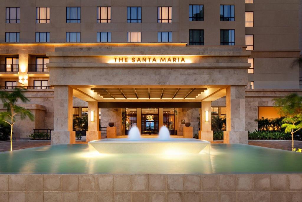Hotel entrance titled 'The Santa Maria' with a lit canopy and water fountain in front at dusk