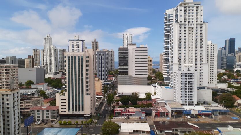 City skyline with white high-rise buildings under a blue sky, viewed from street level.