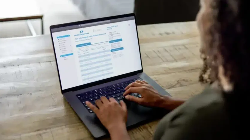 Person typing on a laptop at a wooden table, with an online banking page on the screen