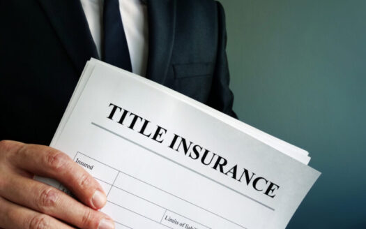 Man in a suit holding a document labeled 'TITLE INSURANCE' at an angle, showing policy form.