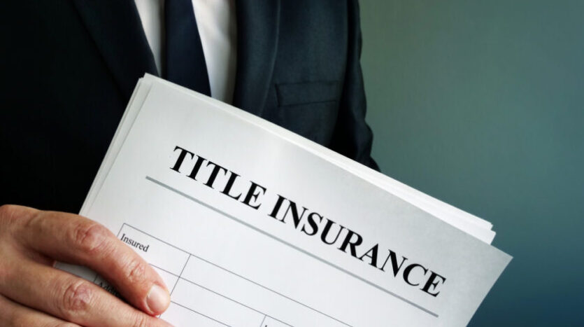 Man in a suit holding a document labeled 'TITLE INSURANCE' at an angle, showing policy form.