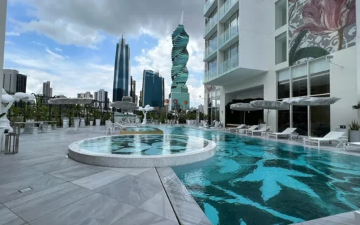 Rooftop swimming pool with a circular hot tub, white lounge chairs and umbrellas, potted plants, and a city skyline of tall buildings in the background.