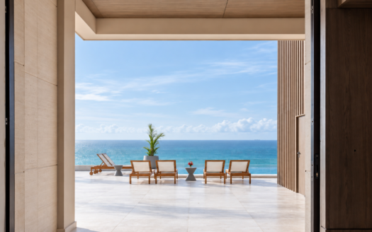 Terrace overlooking the ocean with four wooden lounge chairs and small side tables, blue sea and sky beyond.