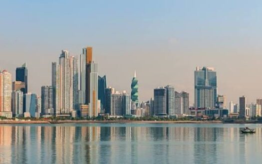 City skyline along a calm body of water with reflections and a small boat on the right.