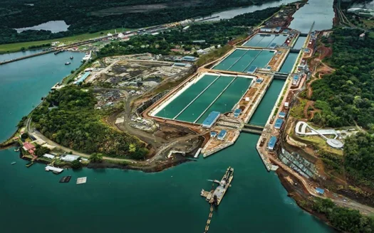 Aerial view of a large water treatment plant with multiple green rectangular basins on a peninsula by the water, surrounded by trees and roads.